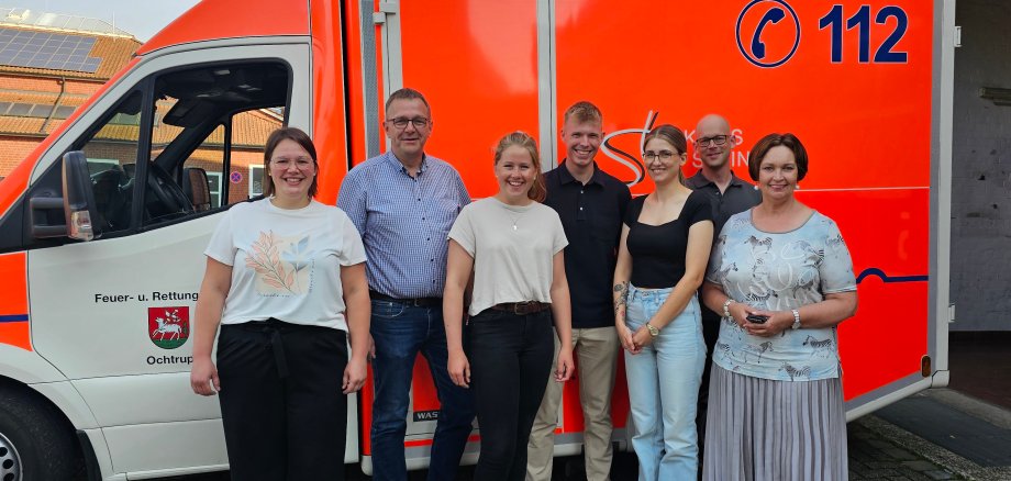 Sie sehen: eine Gruppe von Menschen vor einem Rettungswagen. (V.l.: Ausbildungsleiterin Teresa Stauvermann, Fachbereichsleiter Holger Brüggemann, Hannah Brinkmann, Nico Römer, Aileen Derks, Rettungswachenleiter Roman Beunink und Bürgermeisterin Christa Lenderich)