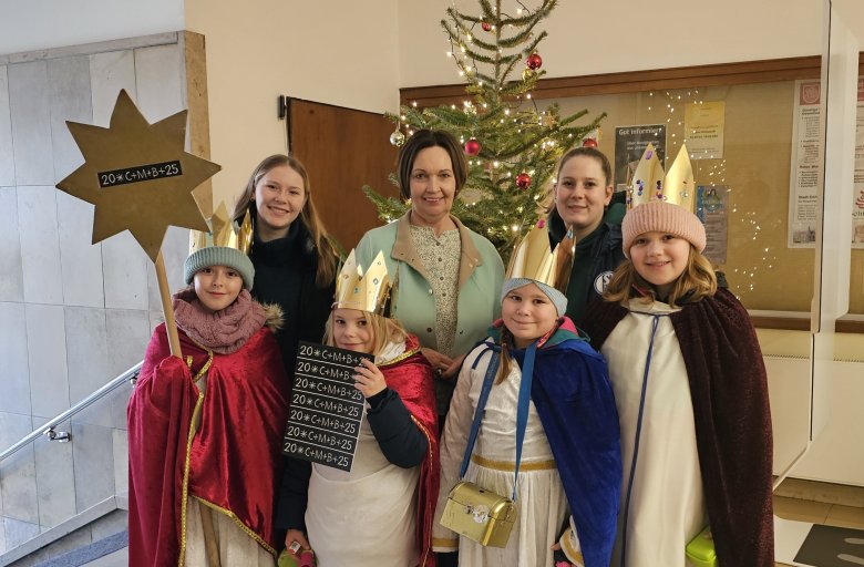 Sie sehen: eine Personengruppe vor dem Weihnachtsbaum im Foyer des Rathauses: Bürgermeisterin Christa Lenderich mit den Sternsingern und ihren Begleiterinnen von St. Lambertus.