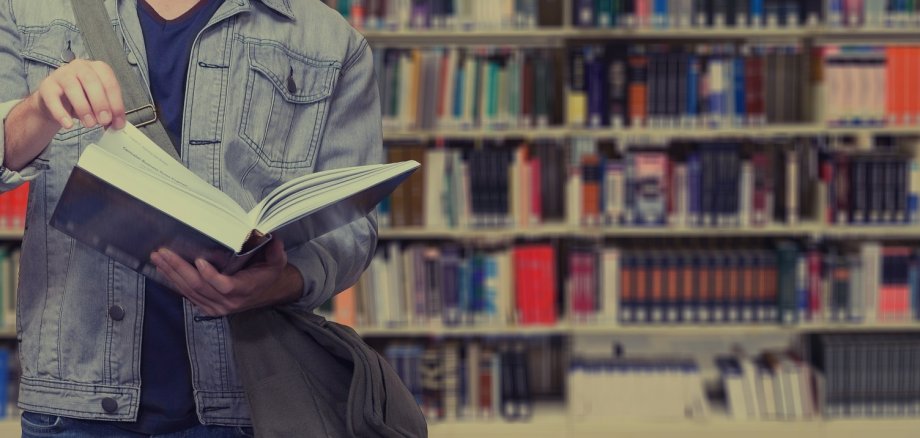 Sie sehen: eine Person mit einem aufgeschlagenen Buch vor einem Bücherregal