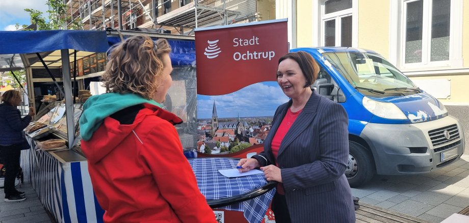 Sie sehen: Zwei Personen im Gespräch an einem Stehtisch: Bürgermeisterin Christa Lenderich auf der Wochenmarktsprechstunde