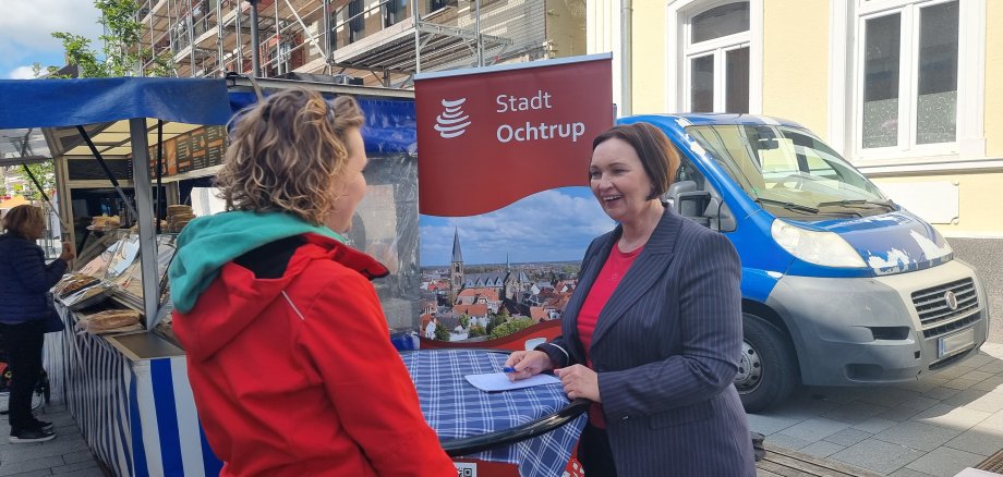 Sie sehen: Zwei Personen im Gespräch an einem Stehtisch: Bürgermeisterin Christa Lenderich auf der Wochenmarktsprechstunde